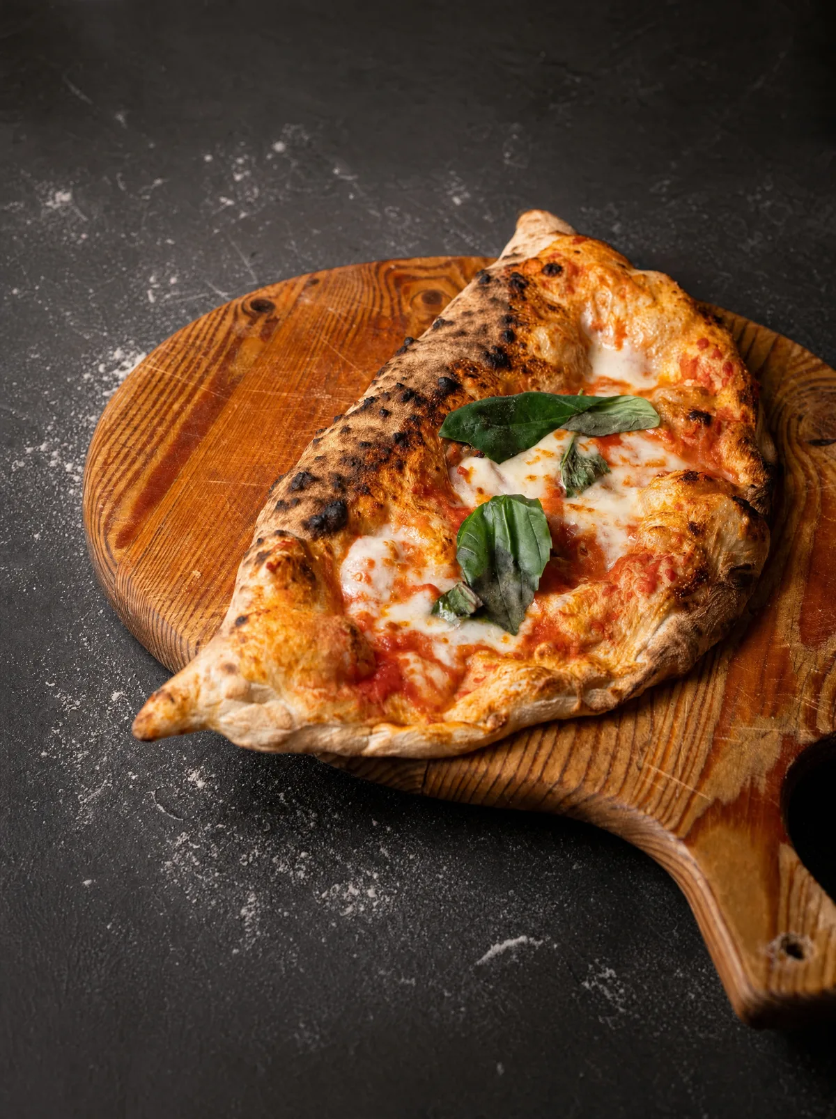 Il nostro calzone al forno sul tagliere di legno, con pomodoro, fior di latte filante e basilico